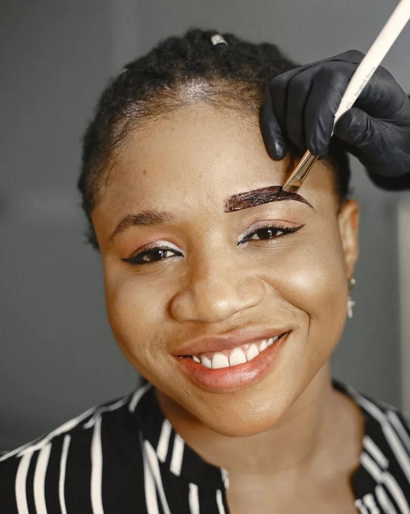 A client smiling while an eyebrow tint is brushed on